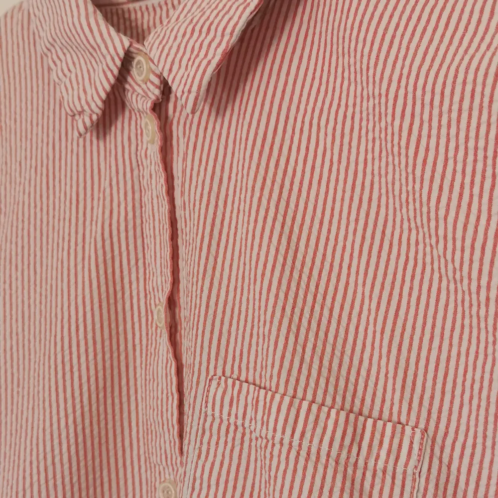 Kortärmad, randig skjorta i bäckebölja. Vit och röd. Uppvikta ärmslut. 100% bomull, kraftig kvalitet.  Längd 55 cm. . Blusar.