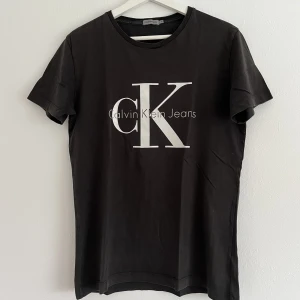 T-shirt - Fin tröja i en lite mörk gråaktig nyans. Tröjan är fint skick men har lite slitage på trycket, syns tydligare på bild 3. 