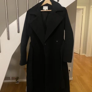 Svart lång kappa - Snygg svart kappa perfekt till höst/vintern. Stl 42/M och går till under knäna på mig som är 172cm. Jättebra skick inga defekter. 