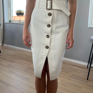 Vit jeanskjol med skärp - Jättefin vit jeanskjol med hög midja och skärp. Knäpps med knappar fram. Vadlång. Lite liten i strl skulle jag säga. Oanvänd.