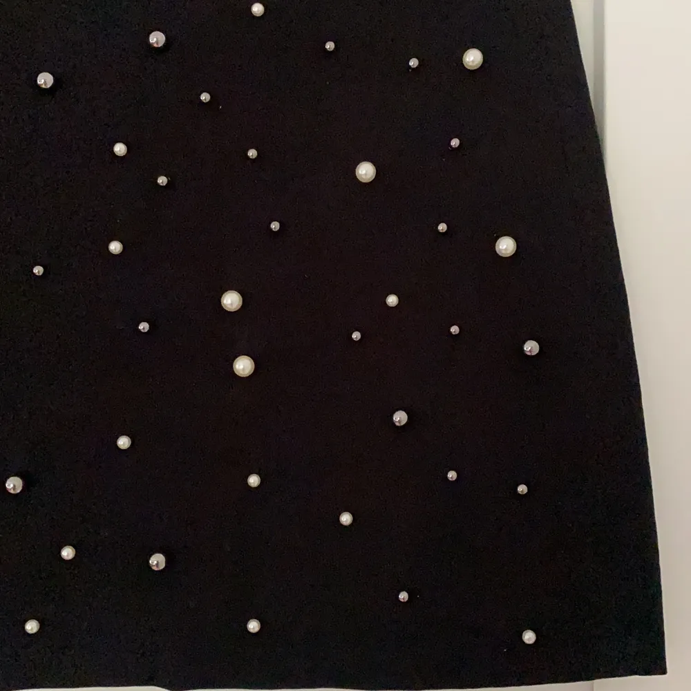Supersnygg svart kjol från New Yorker. På kjolens framsida finns pärlor fast sudda i olika storlekar samt på baksidan är det helt svart. Kjolen är i mocka material samt att det finns en dragkedja som man drar upp på baksidan (den syns knappt). Kjolen kort och i väldigt bra skick! . Kjolar.