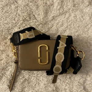 Marc Jacobs Snapshot - Säljer denna super fina och trendiga väskan som är i jättebra skick! Väskan är beige/vit med guldiga detaljer. Väskan är i äkta läder. Bandet går att ta av och går att justera till önskad längd! Bandet är svart/vitt/guldigt. Väskan har två olika fack. Pris kan diskuteras!! Kontakta mig för fler bilder!❤️❤️Nypris 3749 kr!