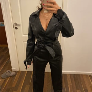 Skinn jumpsuit  - Säljer denna svarta skinn jumpsuiten. Den sitter skit snyggt på, den har en dragkedja och två knappar och även ett band runt midjan och runt händerna. Den går hela vägen ner till fötterna. 