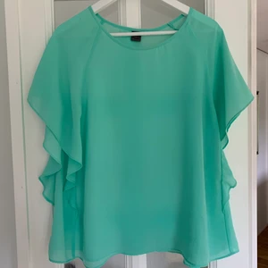 Blus - En turkos blus, väldigt tunn så man ser lite igenom. Men i väldigt fin skick och volanger på sidorna vid armen 