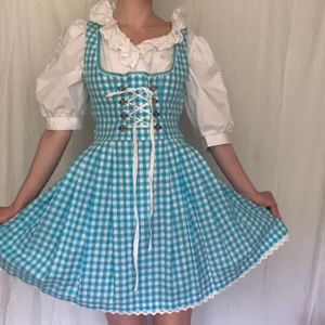 Blå milkmaid klänning dirndl oktoberfest - Säljer denna drömmiga milkmaid klänningen (drndl), då den ej kommit till användning. Den är vit och blårutig, med vita spetsdetaljer och korsett/snörning där fram. Ger mig lite Alice i underlandet/ cottagecore vibes. Stl 36, skulle säga att den passar s-m typ. Perfekt skick (Obs blusen ingår inte)