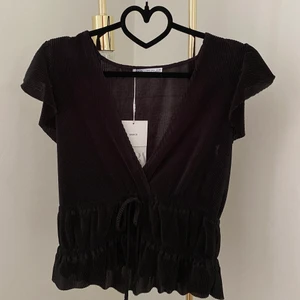 Ny volangtopp från Zara - Säljer denna helt nya svarta volangtoppen från Zara. Tyget är lite plisserat, och toppen har knytdetaljer kring midjan. ✨🦋🌸