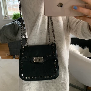 Väska med nitar  - Liten väska med nitar och kedja! Går att ha både över axeln och som cross body! Några nitar har lossnat och finns några sminkfläckar på innerfodret, men inget man tänker på tycker jag 💕💕💕 bud på 150!