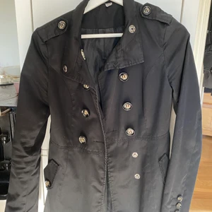 Tynre höstkappa  - En jättefin lite tynre höstkappa som passar perfekt att ha allt från t-shirt till tjocktröja under utan problem! Passformen gör att din midja syns jättefint där den är insydd och när man knäpper den sitter den som en smäck! Säljer p.g.a att den blivit för liten runt axlarna för mig, den är väl använd men den ser inte sliten ut. Har haft ett hål i en inre ficka men det har blivit igensytt. Köparen står för frakten!