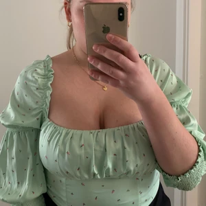 Blommig Blus från H&M divided, strl 44 - Turkos glansig blus med rosa blommor på. Den är lite croppad, slutar vid midjan på mig ungefär. (Är 169cm lång) Storlek 44 från H&Ms divided avdelning. Alltså är tröjan 44 men mer som en 40/42. Den är helt oanvänd, enbart testad. Den har resår i hela ryggen så den är stretchig och går lätt på. Ärmarna är 3/4 långa och har en mudd av resår. Mycket skön och lätt.