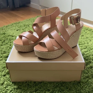Michael Kors högklackade skor - Supersnygga beiga högklackade skor/sandaler från Michael Kors i läder. ALDRIG ANVÄNDA. Det är en platåsko med rep runt hälen som accentuerar det lena lädret och kan ge både en avslappnad samt uppklädd look baserat på hur den kläs. 