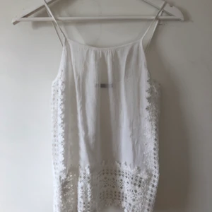 Vit sommartopp i spets - Ett linne i väldigt tunt material, lite genomskinligt. Spetslängst sidorna. Icke justerbara axelband. Öppen på sidorna så det är perfekt att ha när det är varmt. Använd 1 gång, i bra skick.