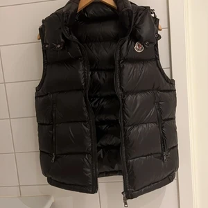 Moncler väst med luva - Köpt i somras på blocket för 4600kr därav har jag sänkt priset. Finns QR kod på insidan som visar att den är äkta och kvitto. Västen är i bra skick.  Säljer eftersom har slutat använda den och ska köpa en annan. Kan gå ner i pris vid snabb affär.