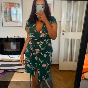 Grön blommig omlottklänning  - V-ringad blommig klänning i färgen grön. Klänningen knyts vid sidan. Nästan helt oanvänd. 