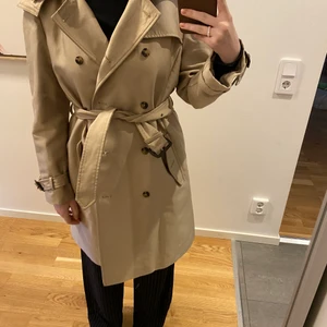 Trenchcoat från Zara strl L - Rejäl och snygg trenchcoat från Zara i strl L (mer som S-M). Väldigt fint skick, men har dock några svarta streck på knytningen (bara skriva om ni vill se bild). Annars i fint skick. Trenchcoaten har en luva, men den går att ta av. På första bilden bärs den av en xs-s o på andra en M. Säljs för 266kr inkl frakt🤍🤍
