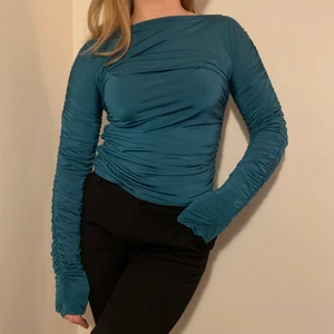 Turkos topp! - Turkos topp som är ruched både längs sidorna och i ärmarna, är från NA-KD. Använd ett fåtal gånger och i nyskick! Jag är 170cm lång och har oftast S/36 i storlek.