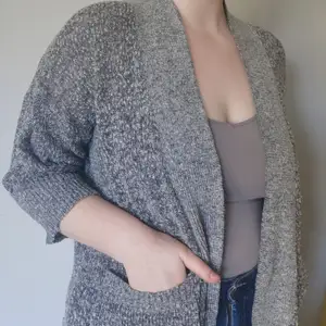 Grey knitted cardigan, it has short sleeves and large pockets. 