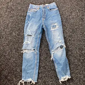 Mörkblåa högmidjade jeans med hål och knapp gylf. Storlek 36