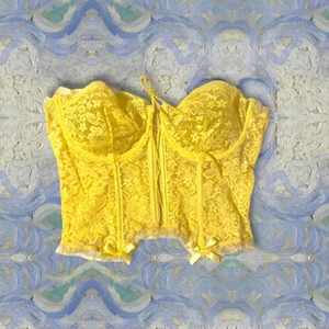 Korsett top - En gul korsett top med snörnings i fram för att spänna den till önskad storlek. Band runt axlarna men man kan klippa bort de elr stoppa undan de. Storlek L. Skulle säga att det är C kupa men skulle kunna passa D. Oanvänd. Frakten ingår i priset. Högst bud vinner plagget. (Sista bilden är lånad)
