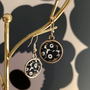 Marimekko Unikko örhängen NYA! - Nya örhängen med Marimekko-motiv (Unikko). Nickeltestad silverfärgad metall. Glas över själva mönstret. Ca 1 cm i diameter. 150 kr eller bud