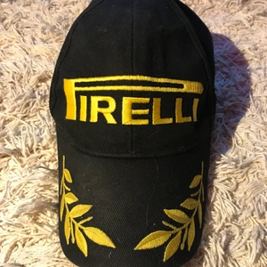 Pirelli Keps - Gul/svart keps från Pirelli, one size. Lapparna på sidan är sydda annars är allt annat broderat. Kardborre spänne bak.