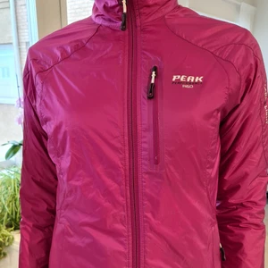 Peak Perfomance Jacka - Lättviktsjacka från Peak Perfomance i cerise färg. Dragkedjor på fickorna och dold dragsko nedtill. Innerficka fi ns också. Slim modell och lätt.