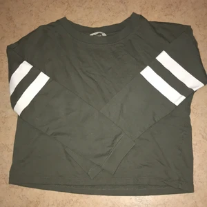 Grön tröja med vita ränder  - Långarmad grön tröja med två vita ränder runt varje överarm. Något kort 