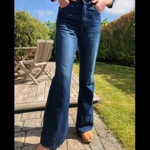 Helt nya 70’s high flare jeans från Levi’s i färgen medium indigo. Hög midja och utsvängda ben i sann 70-talsstil. Jeansen sitter snyggt och kroppsnära kring midja, stuss och lår med vida ben som svänger ut. Oanvända. Jag som har på mig dem i bilden är 172cm lång och väger 60kg. Sitter då en aning löst. 