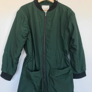 Jacka Monki - Höst/vinterjacka från Monki i en fin, djup grön färg. Quiltat foder och med snören i midjan som går att spänna åt om så önskas. Storlek S.