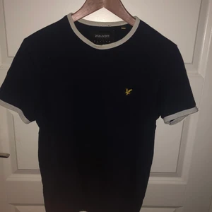 Lyle & Scott t-shirt  - En mörkblå tshirt med vita konturer runt hålen. Tshirten är från Lyle & Scott och är köpt i London i storlek S. Allt är i bra skick förutom i kragen som är lite utnött. Därför säljs den för ett så billigt pris som 50kr!