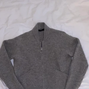Grå stickad kofta med dragkedja  - Koftan går ungefär till naveln och sitter hyfsat tajt på kroppen. Har stora fickor och en fin dragkedja.
