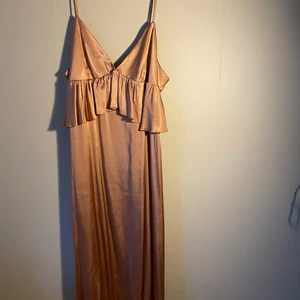 En knä lång siden klänning  - En beige siden klänning med oranga/bruna toner från HM som aldrig är använd. Klänningen är rak men har en ”volang” vid bysten. Den är V-ringad med smala band som är justerbara 