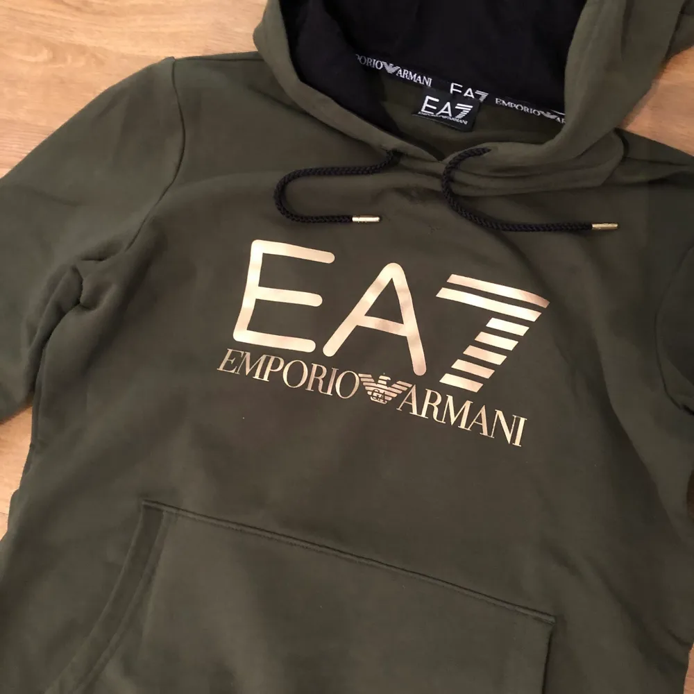 Militärgrön hoodie/tjocktröja från Emporio Armani med gulddetaljer och guldtryck. Mjukt material. Sparsamt använd. Säljer pga att jag har vuxit ur den. Storlek XS. Inköpt för 999kr, säljs nu för 199kr. Först till kvarn!. Hoodies.