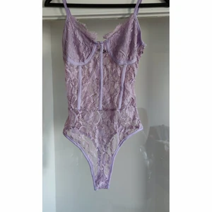 Lila/ljuslila pastell spets bodysuit top - En fin endast testad spets Body med extra tyg vid kuporna , knäpps med knappar vid grenen. Storlek 40 ,passar medium. Från tall kollektion och passar därför längre personer också.