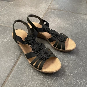 Rieker sandaletter med kilklack  - Säljer mina svarta sandaletter med kilklack från Rieker. De är i väldigt fint skick med fina svarta blommor på som detalj🌸☺️