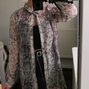 Transparent skjorta  - Grå mönstrad skjorta/skjortklänningen med en öppen detalj på ryggen. Funkar samtliga årstider! Stlk M men passar XS-M beroende på hur lös/tight passform man vill ha. Jag är generellt stlk S för referens.