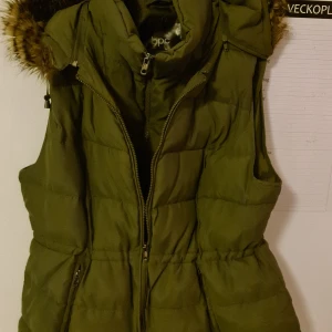 Fodrad väst - En fin fodrad, grön väst med avtagbar luva och justerbar midja i strlk 50 i jättefint skick