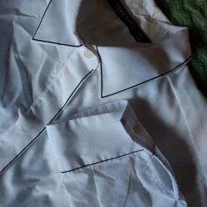 Festlig skjorta🥂 - En festlig skjorta från Zara, med snygga svarta detaljer vid krage, knappar och ärm. Modellen är lite rakare och vidare nedtill. Säljer den då den är lite för liten för mig nu. Bara använd en gång! Köparen står för frakten men kan även mötas upp i gbg💛