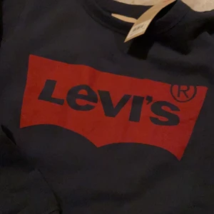 Levi’s tröja - Säljer en Levi’s tröja då den aldrig har kommit till användning, helt ny med lapparna kvar. Marin blå med rött tryck.