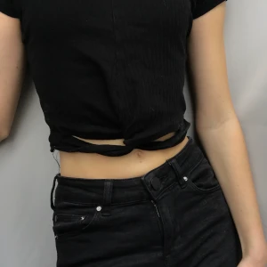 Skön svart croppad shirt från NewYorker! - Använd några få gånger. Den är svart ribbad och den har 2 hål nertill! Väldigt fin men tyvärr för liten 