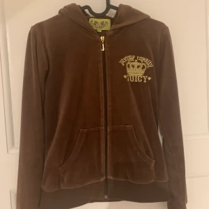 Juicy Couture Hoodie - Brun hoodie i sammet från Juicy Couture. Barnstorlek M, vilket ungefär motsvarar XXS/XS. Den är lite nopprig på muddarna, men de försvinner med noppmaskin. Den har även två små hål, som knappt syns, vid fickorna. Det ena hålet är lagat. Säljes inkl. frakt.