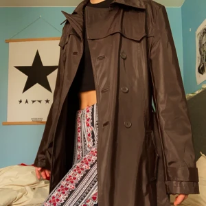 Brun Trenchcoat Kappa - Brun unik PVC-kappa med foder och vackert bälte! Köpt second hand, i fint skick! 🤎