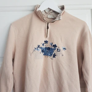 Zip-up tröja - Fin beige zip tröja med blå blommor! Köpt på plick men aldrig använd av mig, syns att den är använd men fortfarande fin. Från axel till slutet av ärmen är den 51 cm
