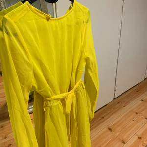 En fin gul klänning med bälte i likadant tyg