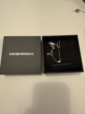 Silverhalsband från Emporio Armani - Snyggt silverfärgat halsband från Emporio Armani med tunn kedja och ett elegant hängsmycke. Kommer i original ask med logga. Perfekt accessoar för att lyfta din outfit och visa din stil.