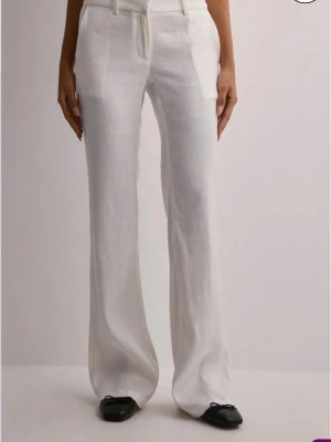 Vita utsvängda linnebyxor - Snygga vita linnebyxor med låg midja och utsvängda ben. Byxorna har bälteshällor och diskreta fickor fram. Perfekta för en avslappnad och stilren look. Tillverkade luftigt linnematerial. Säljer då de tyvärr ej kommer till användning och de är använda en gång. Slutsålda på hemsidan. 