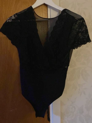 Svart spetsbody med kort ärm - Snygg svart body med djup V-ringning och korta ärmar i spets. 