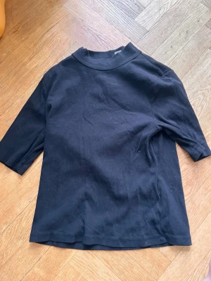 Svart ribbad polotopp - En svart ribbad polotopp med halvlånga ärmar och hög krage. Toppen har en enkel och stilren design som passar till många olika looks. Materialet känns mjukt och stretchigt för en bekväm passform. Passar även M. Skriv gärna för mått! 💕