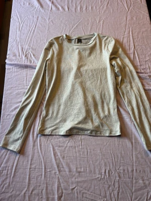 Ljusgrå långärmad topp - En enkel och stilren ljusgrå långärmad topp med rund halsringning. Tillverkad i ett mjukt och stretchigt material som passar perfekt till alla typer av outfits. Snygg att bära både till jeans och kjol.