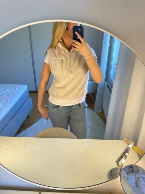 Beige fleeceväst med half zip - Mysig beige fleeceväst med krage och half zip framtill. Västen har en bröstficka med dragkedja och en avslappnad passform. Perfekt att slänga över en t-shirt för en casual look. Köptes för 300kr  . Är i strl Xs men sitter mer som en S