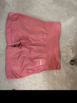Rosa högmidjade shorts från AYBL - Snygga rosa shorts från AYBL med hög midja och ribbad linning. Perfekta för träning eller chill dagar. Tillverkade i ett stretchigt syntetmaterial som sitter skönt och formar sig efter kroppen. Diskret logga på benet för en clean look.